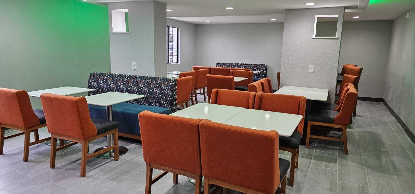 A restaurant with booths and tables, featuring a geometric patterned bench, wooden chairs, and a tiled floor.