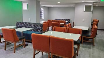 A restaurant with booths and tables, featuring a geometric patterned bench, wooden chairs, and a tiled floor.