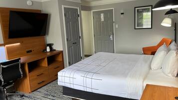 Habitación de hotel con una cama grande, un televisor de pantalla plana montado en una consola de madera, un escritorio con una silla y una lámpara de escritorio.