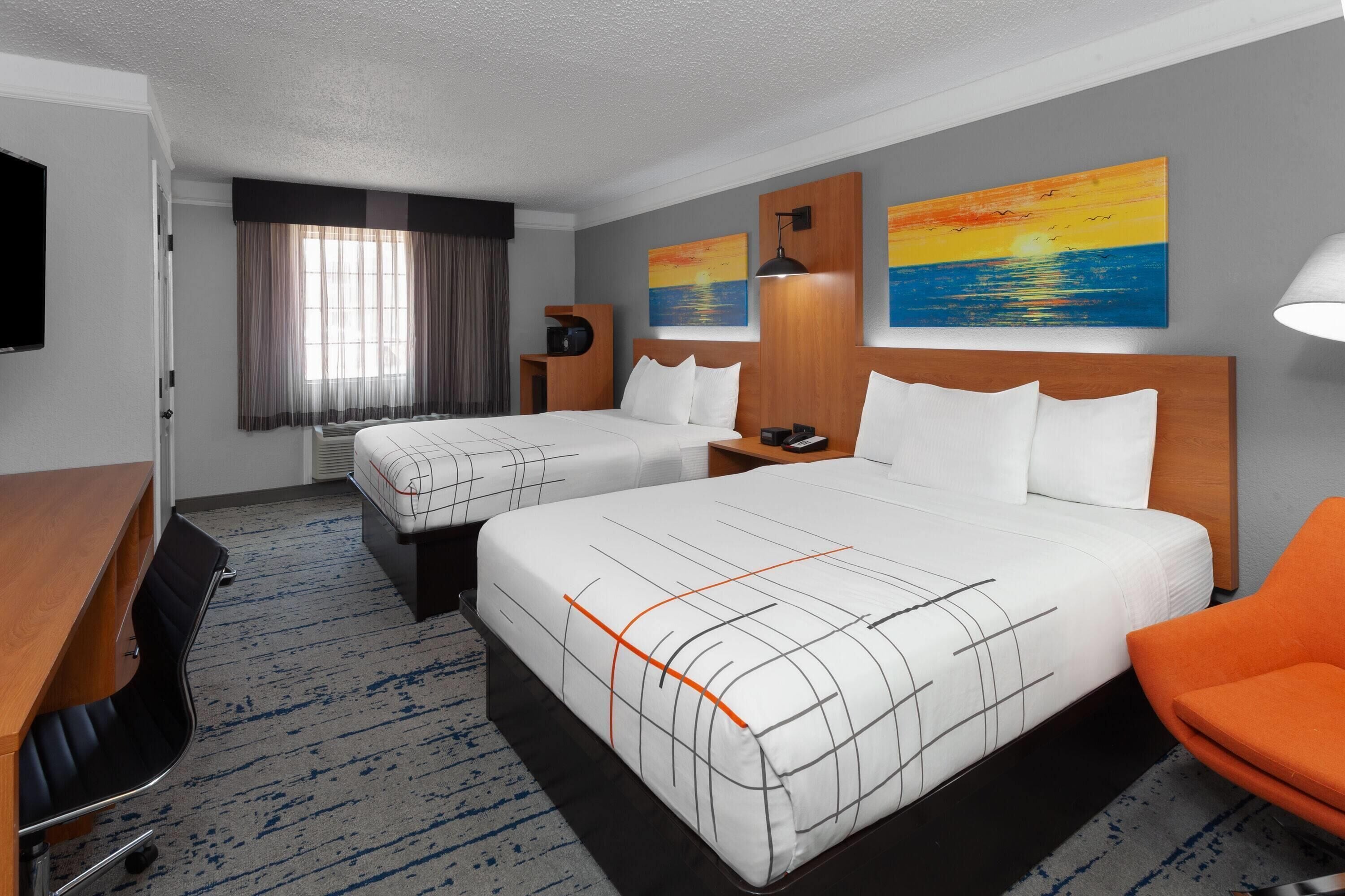 A hotel room with two beds, a desk, a chair, and artwork on the walls.