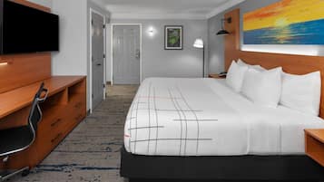 Habitación de hotel con una cama grande, un escritorio con silla, televisor de pantalla plana, un cuadro en la pared y una puerta que da a otra habitación.