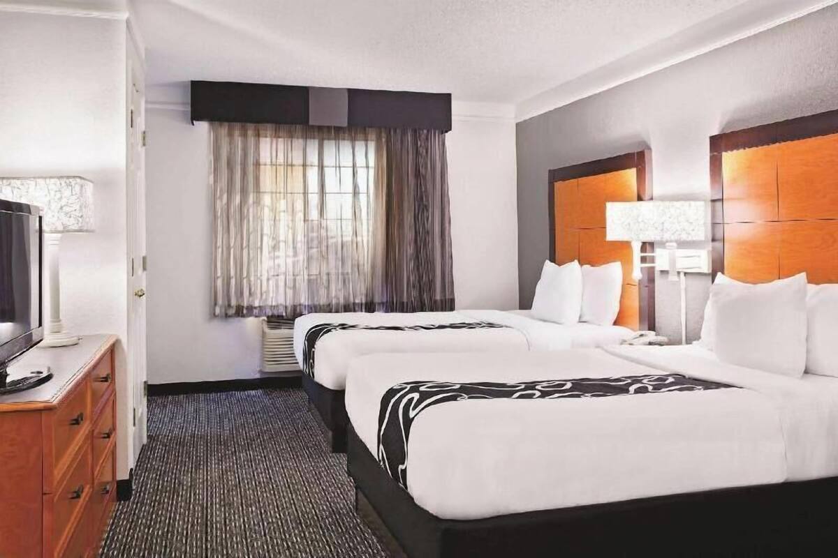A hotel room with two beds, a TV, a desk, and a window with curtains.