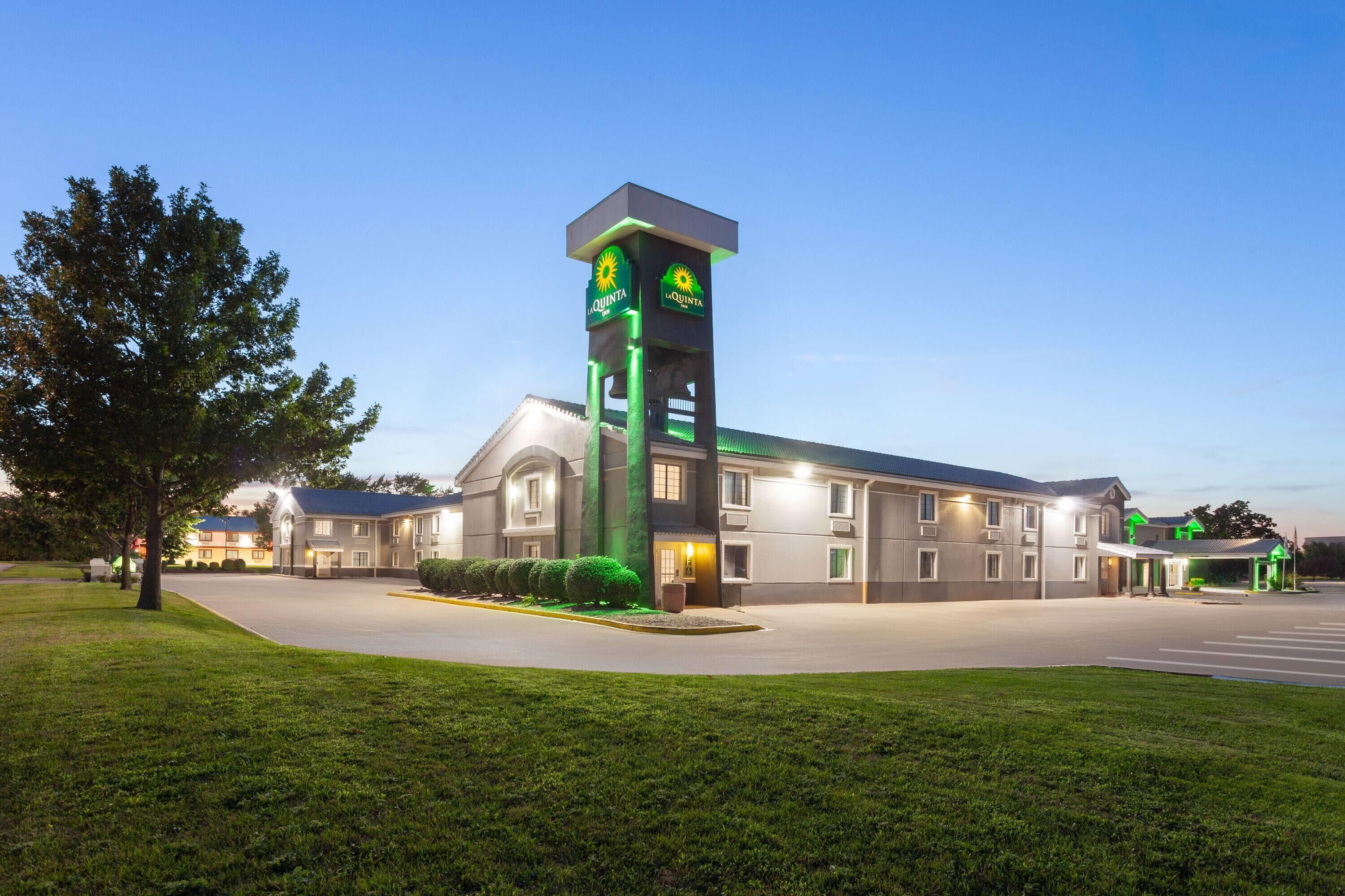 A hotel with a prominent tower, a parking lot, and well-maintained lawns.