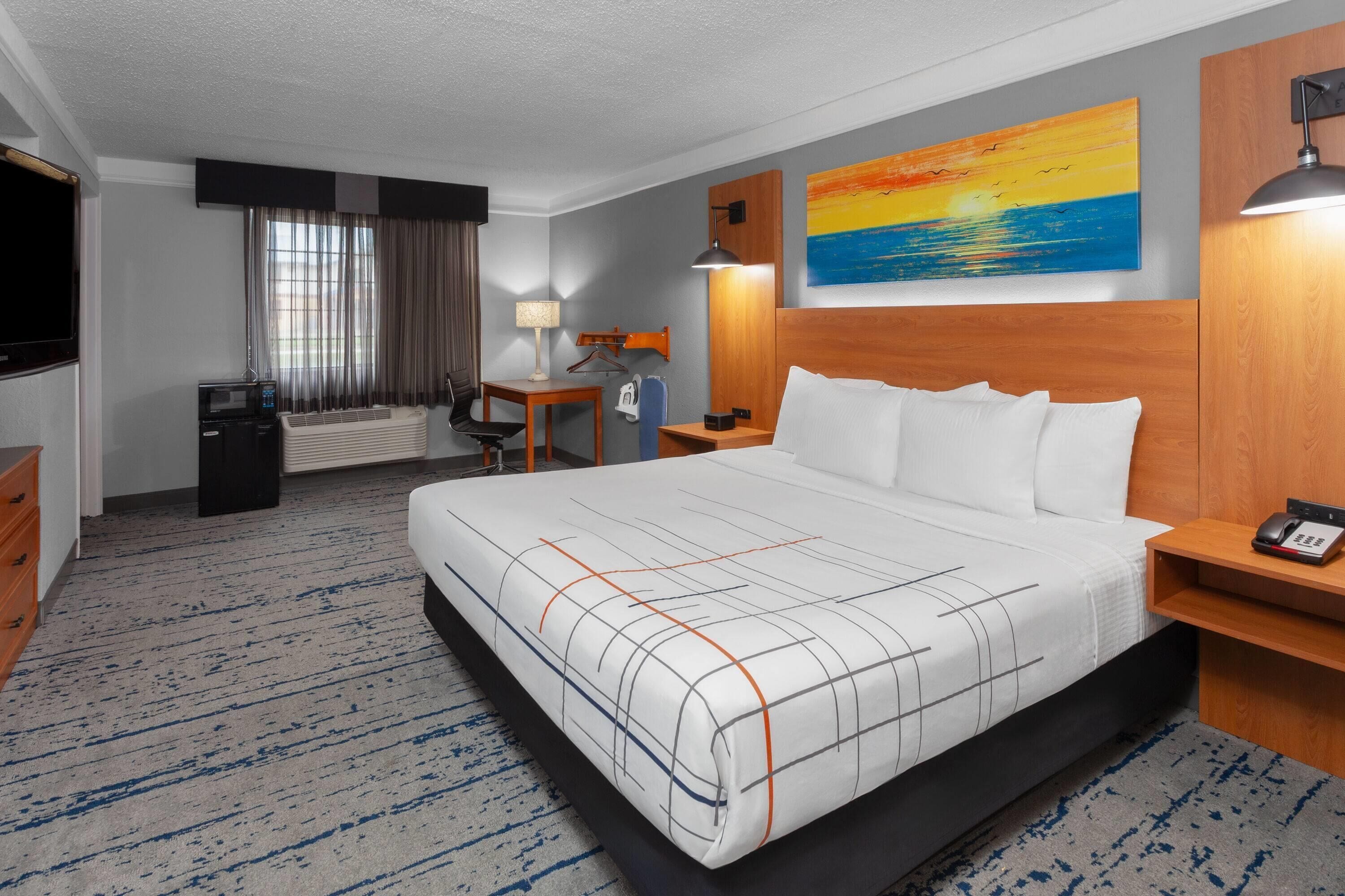 Une chambre d’hôtel avec un grand lit, un bureau, une chaise, une télévision, un radiateur et un tableau au mur.