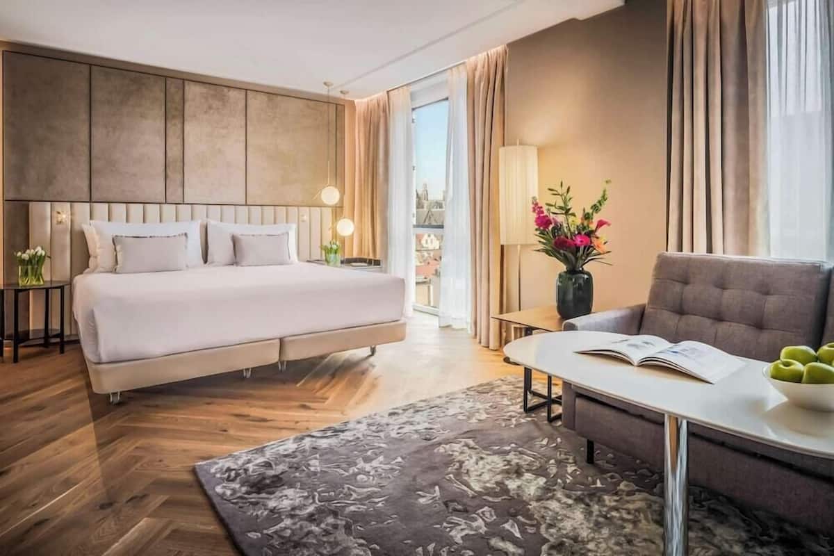 A hotel room with a bed, a sofa, a coffee table, and a view of the city.