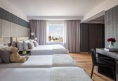 A hotel room with two beds, a desk, and a view of the city.