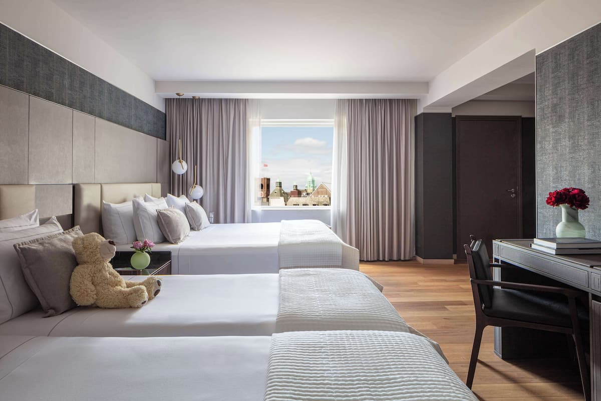 A hotel room with two beds, a desk, and a view of the city.
