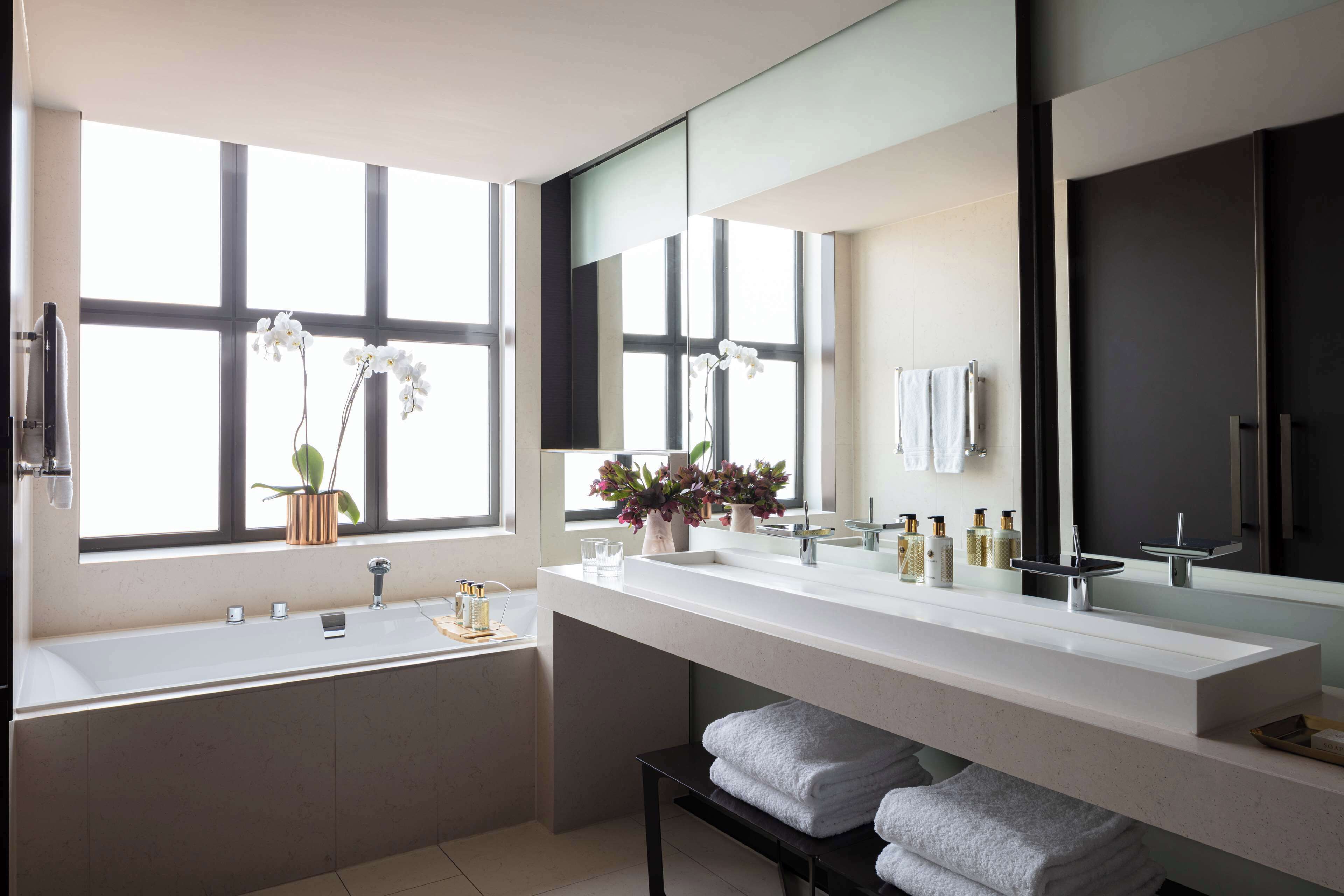A modern bathroom with a large window, a bathtub, a vanity with a mirror, and a towel rack.