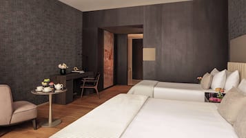 A modern hotel room with a large bed, a desk with a chair, a small table with a vase of flowers, and a large window.