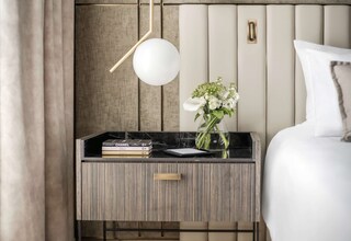 A modern bedroom with a wooden nightstand, books, a vase with flowers, and a bed with white bedding.
