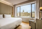 A hotel room with a large bed, a small round table, and a view of a historic building through the window.
