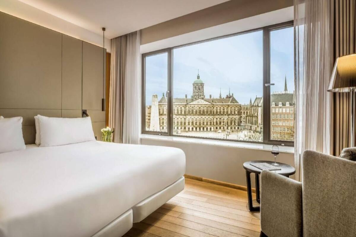 A hotel room with a large bed, a small round table, and a view of a historic building through the window.