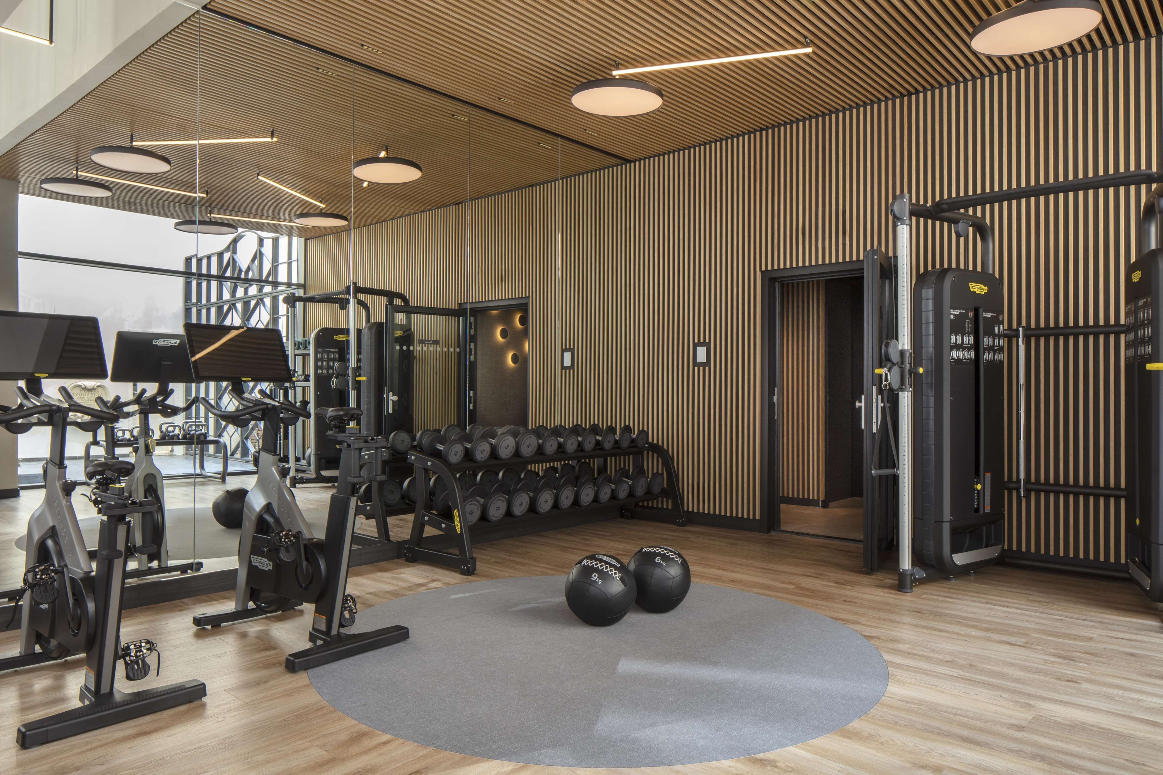 Un gimnasio moderno con equipamiento de ejercicio, un muro espejado y un diseño de pared de madera.