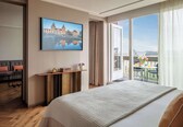 A hotel room with a large bed, a desk, a sofa, and a balcony with a table and chairs.