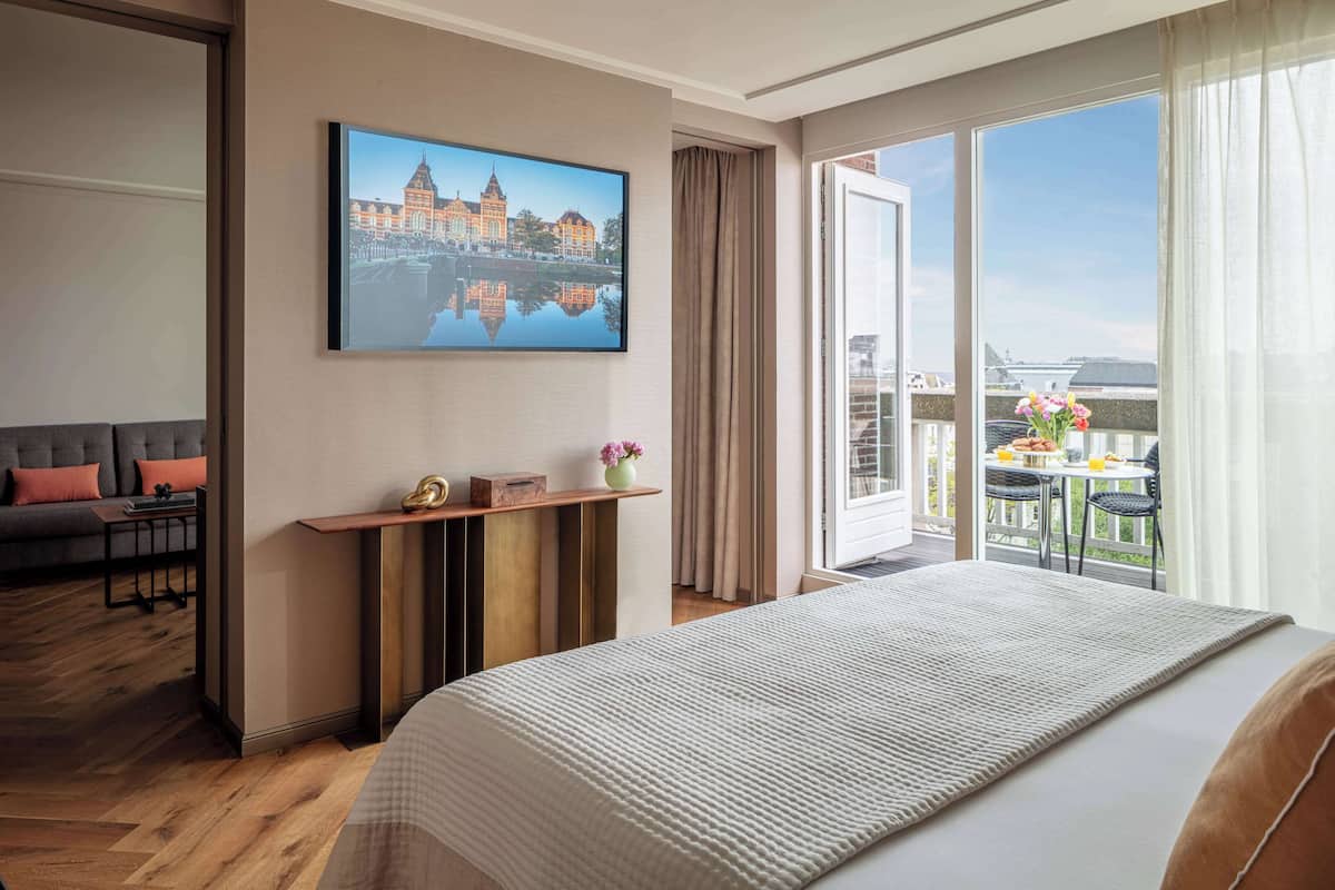 A hotel room with a large bed, a desk, a sofa, and a balcony with a table and chairs.