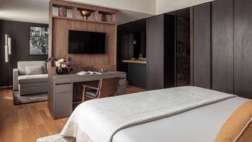 Une chambre d’hôtel moderne avec un grand lit, un bureau avec une chaise, un téléviseur fixé sur un panneau en bois et un canapé.