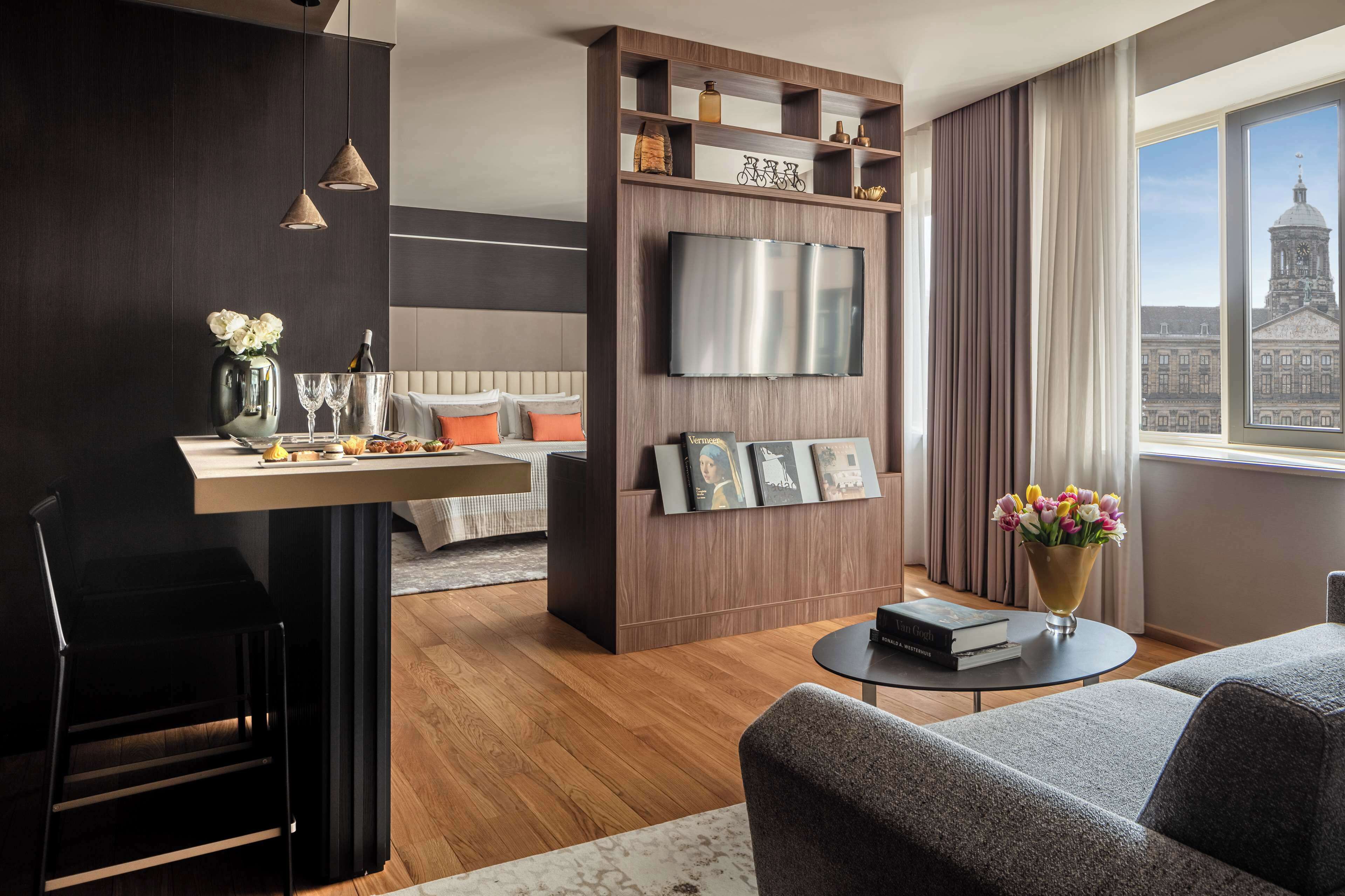 Una sala de estar moderna con comedor, un televisor montado en una pared de madera y vista a un edificio a través de un ventanal grande.
