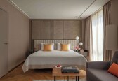 A modern hotel room with a large bed, a bedside table with a lamp, a sofa, and a wooden coffee table.