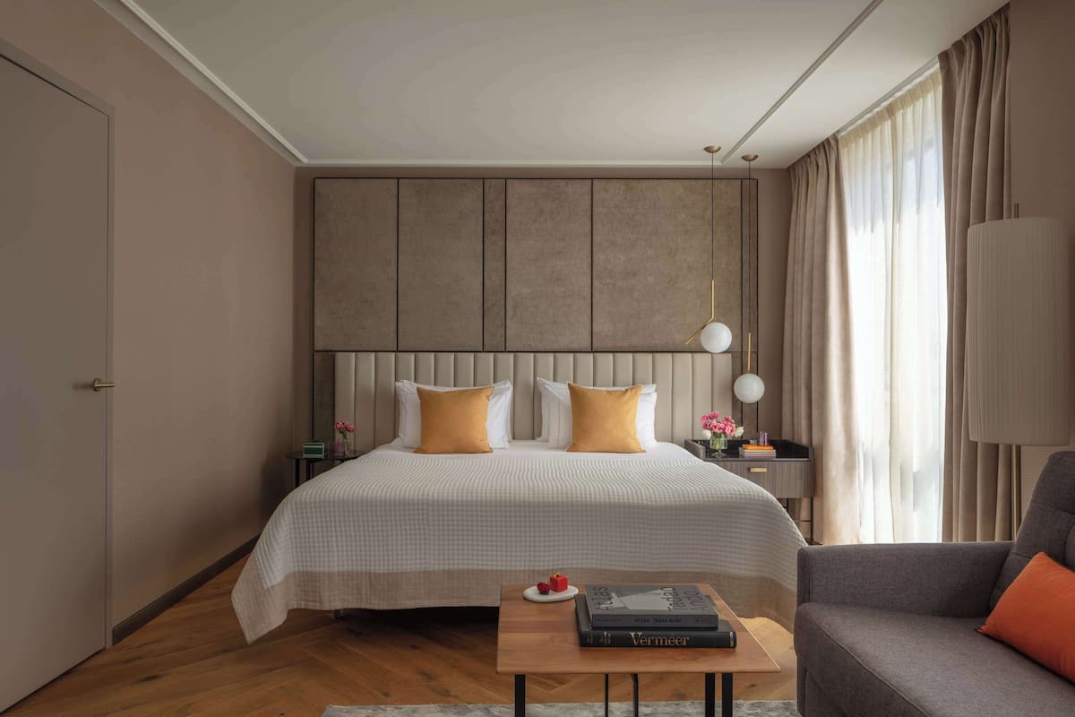 A modern hotel room with a large bed, a bedside table with a lamp, a sofa, and a wooden coffee table.
