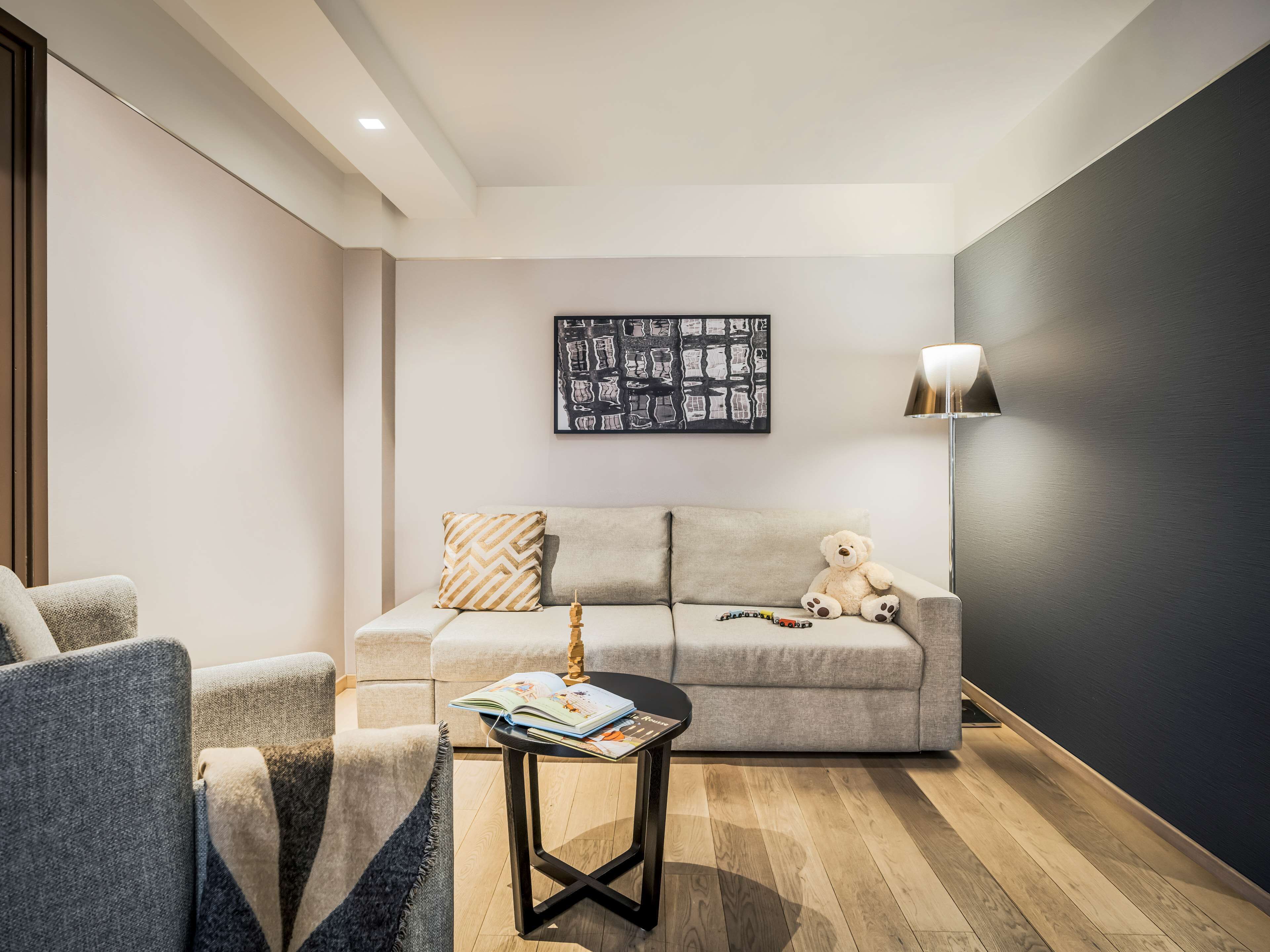 Un salón moderno con un sofá gris, una mesita redonda con un libro, un osito de peluche y una lámpara de pie.