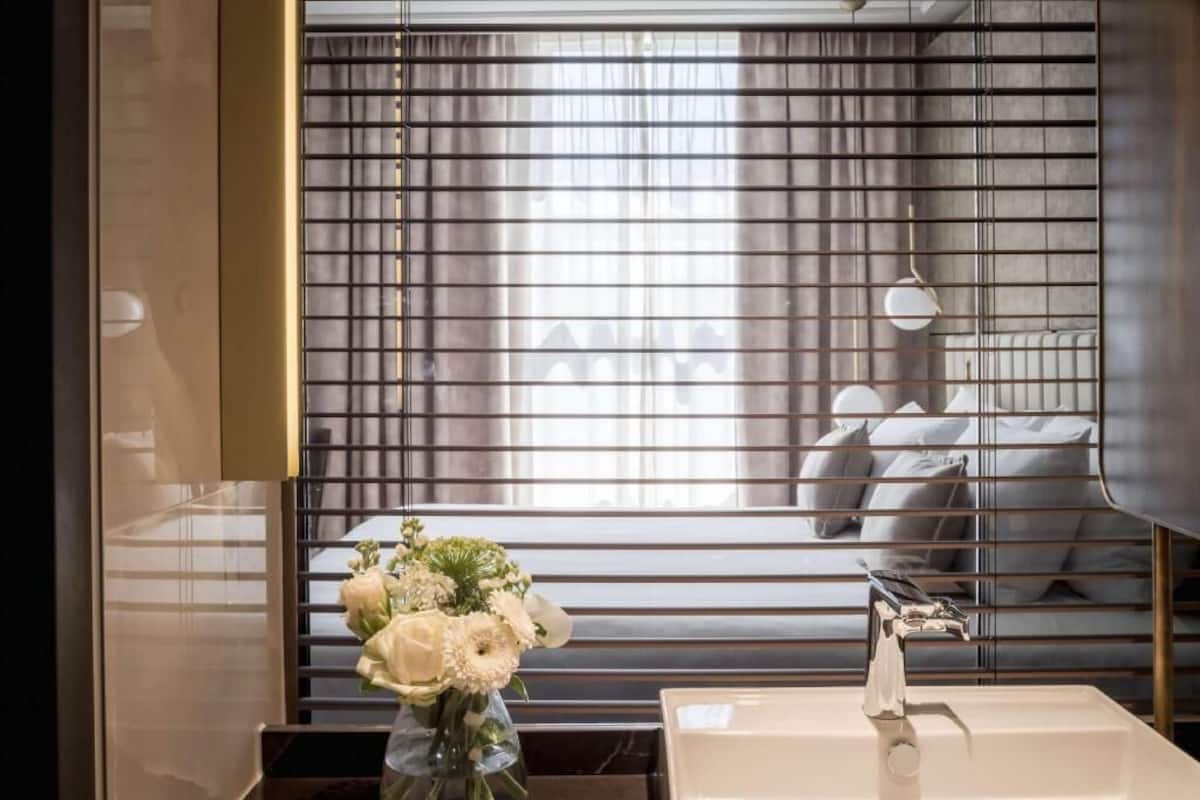 A modern bathroom with a large mirror, a white sink, and a vase of flowers.
