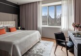 A modern hotel room with a large bed, a desk, and a view of a historic building.