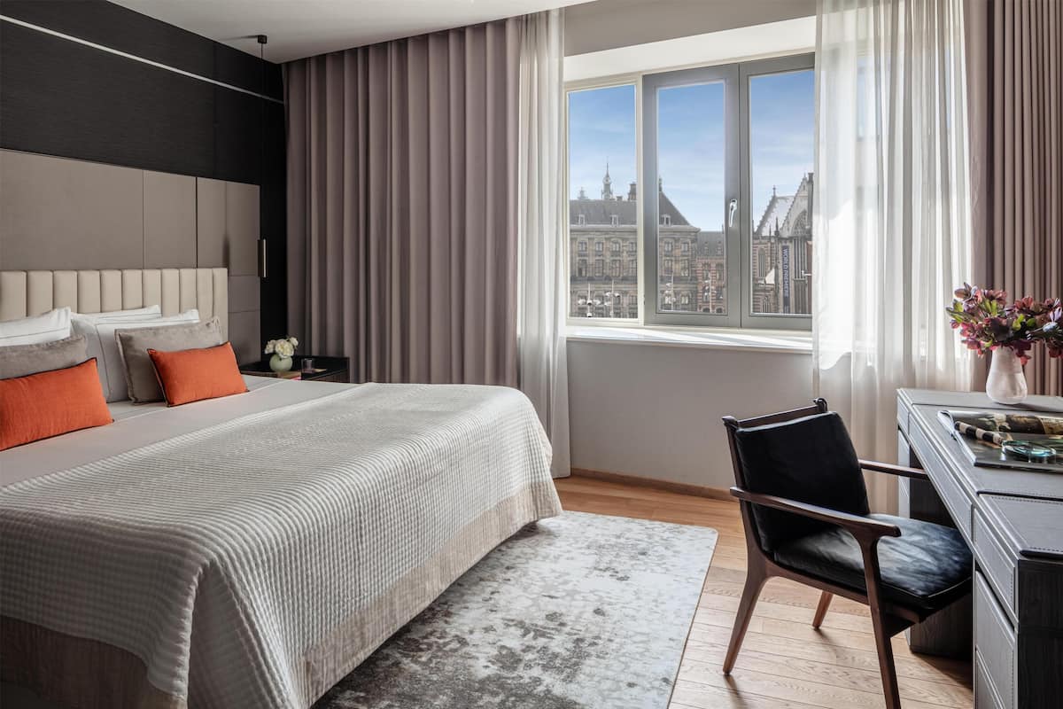 A modern hotel room with a large bed, a desk, and a view of a historic building.
