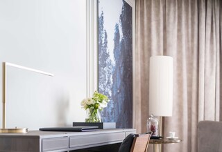 A modern hotel room with a desk, chair, and a large window with a view of trees.