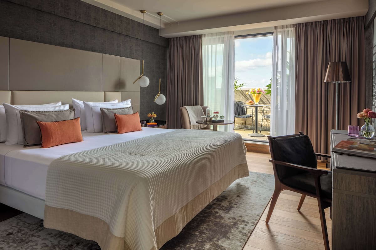 A hotel room with a large bed, a desk, a chair, and a view of the outdoors.