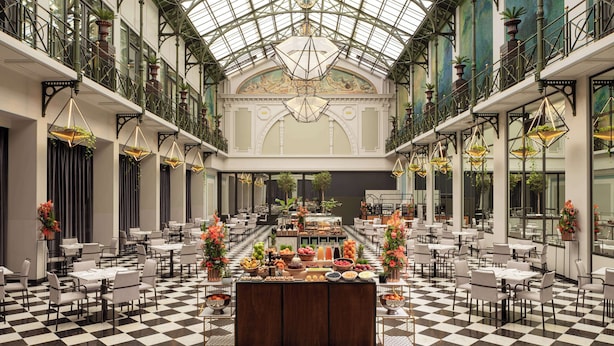Un vaste atrium doté d’un sol à carreaux, d’un buffet central proposant une variété de plats et d’un plafond haut surmonté d’une coupole de verre.
