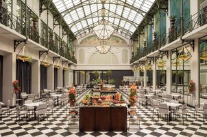 A spacious atrium with a checkered floor, a central buffet with various food items, and a high ceiling with a glass dome.