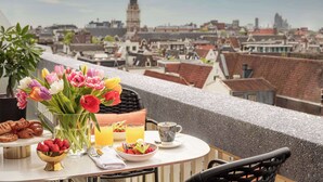 Une table dressée avec des aliments pour le petit-déjeuner, un vase de fleurs et une vue sur un paysage urbain avec une tour imposante.