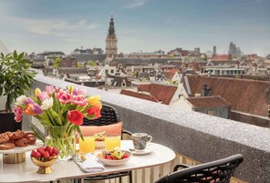 A table with breakfast items, a vase of flowers, and a view of a cityscape with a prominent tower.