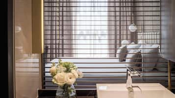A modern bathroom with a large mirror, a white sink, and a window with blinds.