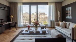 Un salon moderne doté d’une grande fenêtre, d’un canapé, d’une table basse avec des livres et un vase de fleurs, et offrant une vue sur la ville.