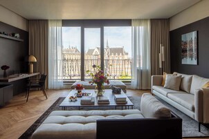 A modern living room with a large window, a sofa, a coffee table with books and a vase of flowers, and a city view.