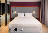 A modern hotel room with a large bed, bedside tables, a mirror, and a small table with a cup and glasses.