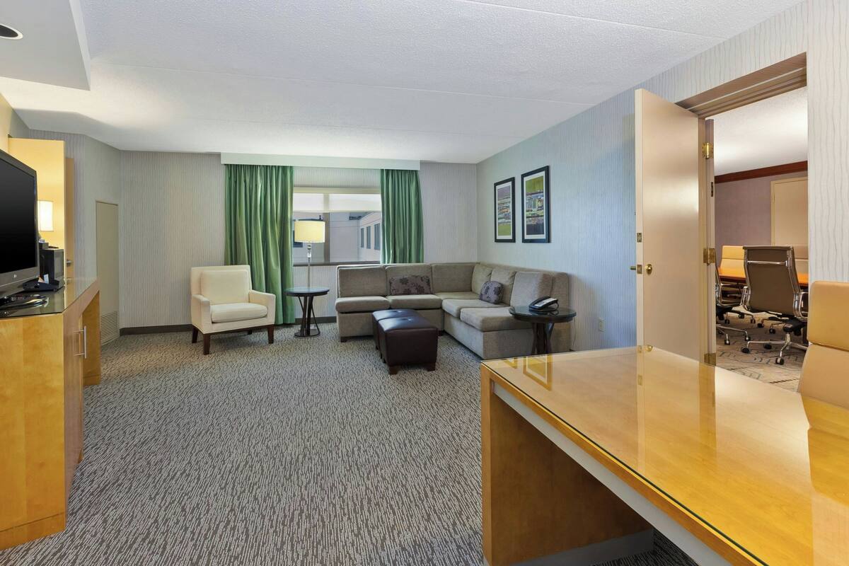 A hotel room with a sofa, armchair, small table, and a desk.