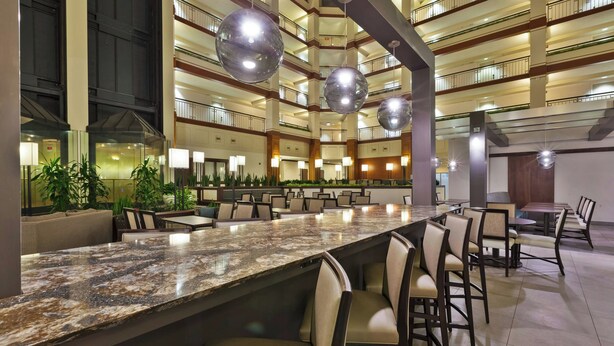 A spacious hotel lobby with a central bar area, multiple dining tables, and a high ceiling with hanging spherical lights. - Hotel Auburn Hills (Auburn Hills)