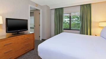 A hotel room with a bed, a television on a wooden dresser, a window with curtains, and a door.