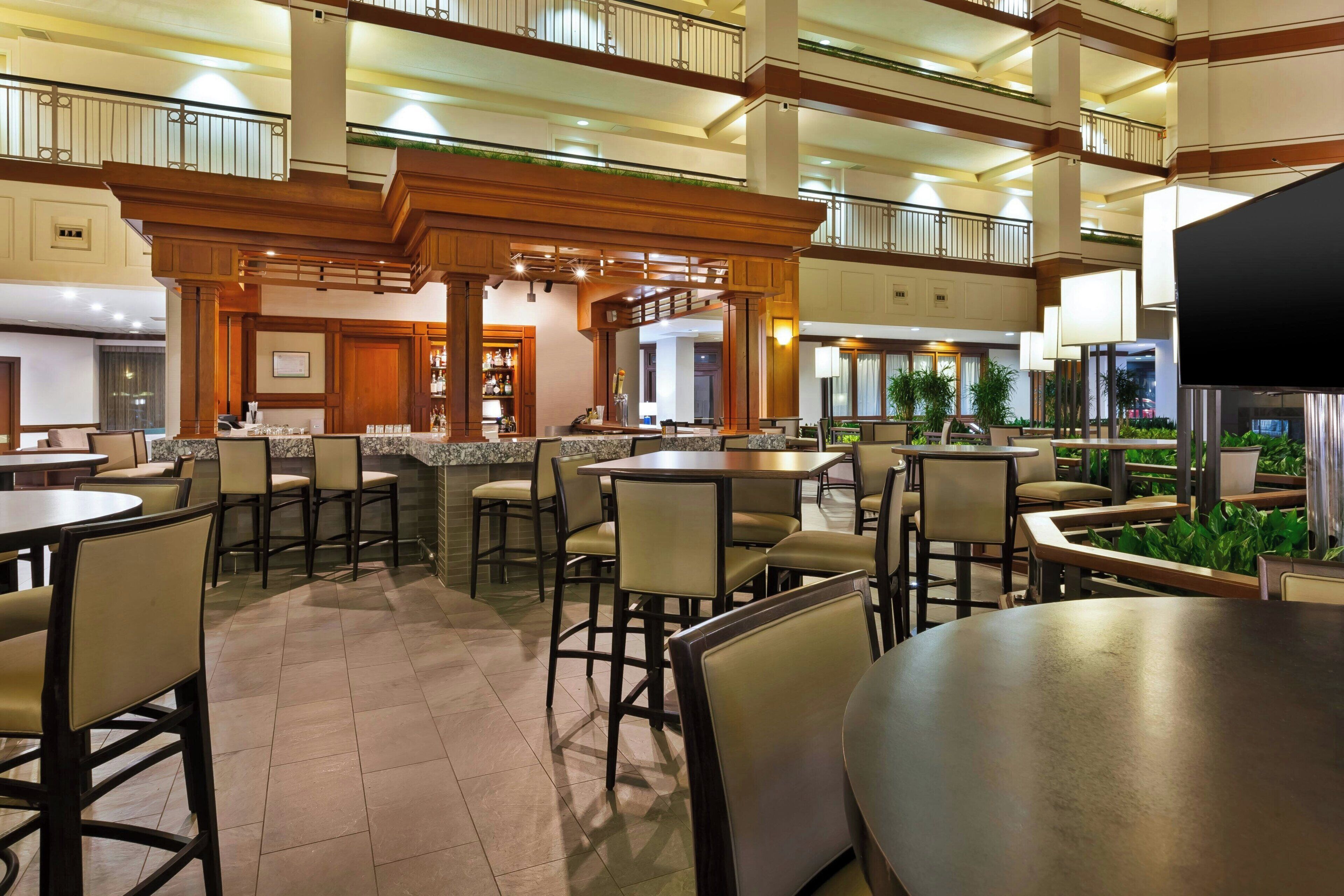 A spacious indoor dining area with multiple tables and chairs, a bar area, and a view of the outdoor garden.