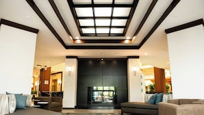 A lobby with a modern design, featuring a large fireplace, comfortable seating, and a skylight above. - Hotel Auburn Hills (Auburn Hills)
