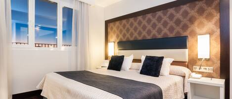 A hotel room with a large bed, two bedside tables, a nightstand, and a window with curtains.