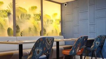 Un comedor con una mesa larga, sillas estampadas, un banco acolchado y una pared con un panel decorativo.