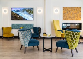 Eine moderne Lobby mit einem großen Fernseher, der eine verschneite Berglandschaft zeigt, bequemen Sitzgelegenheiten mit ungewöhnlicher Polsterung und einem Kamin.