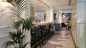 A modern interior with a long reception area, bar seating, and a staircase leading to an upper level. - Hotel Gran Versalles (Madrid)