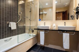 Ein modernes Badezimmer mit einer gläsernen Duschkabine, zwei Waschbecken und einer Badewanne.