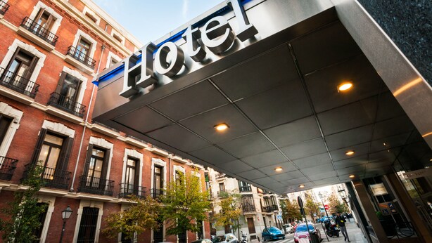A hotel entrance with a modern sign, traditional brick buildings, and a covered walkway. - Hotel Gran Versalles (Madrid)
