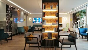 A modern lobby with a central bookshelf, seating area, and a staircase. - Hotel Gran Versalles (Madrid)
