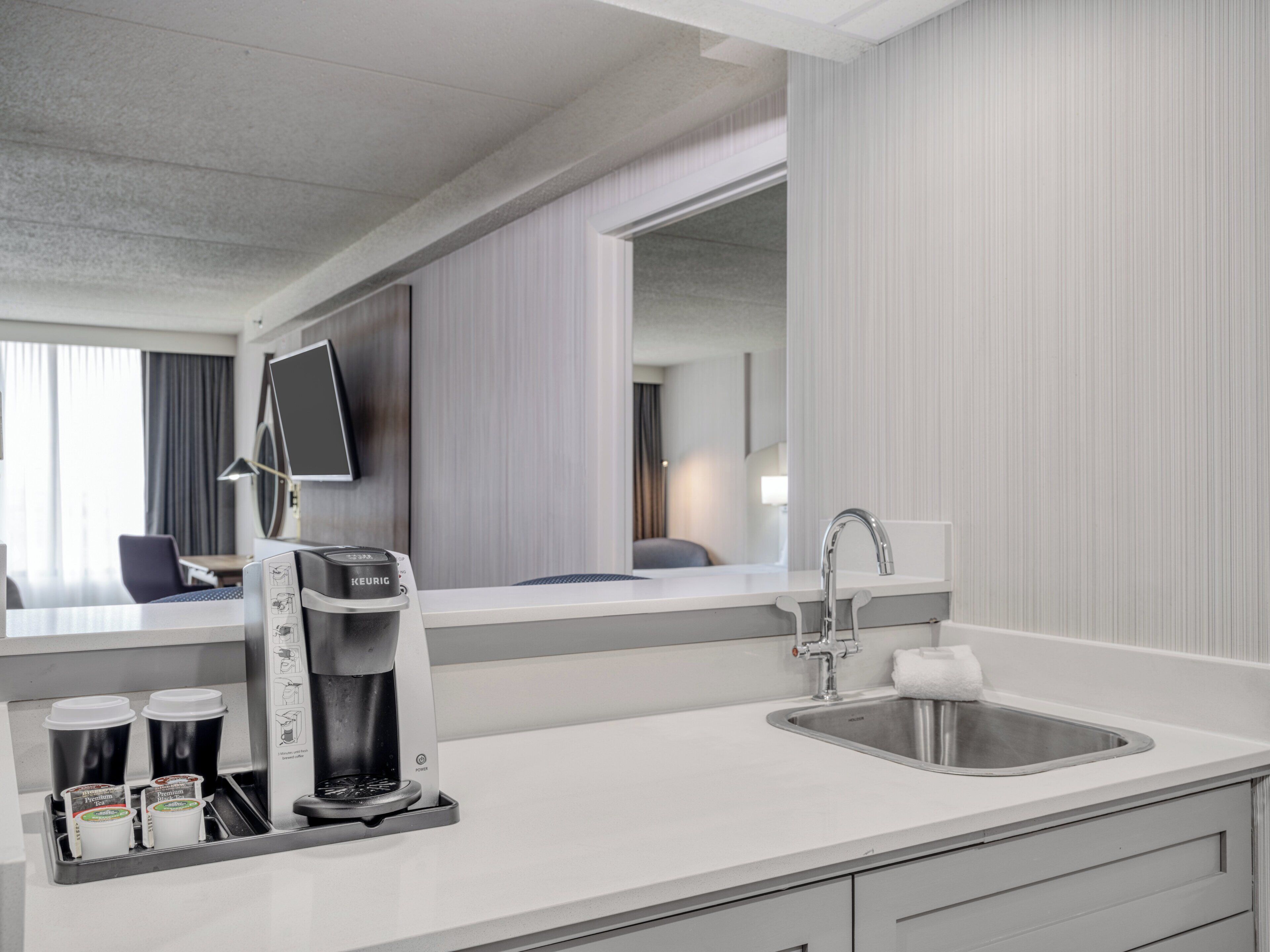 A modern hotel room with a coffee maker, a sink, and a mirror.